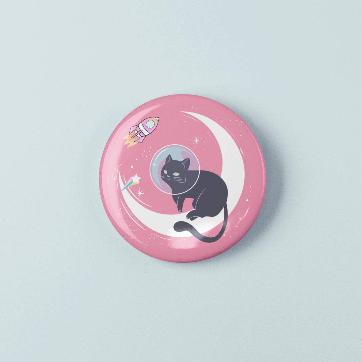 Pink button badge with a cat in a space suit on a crescent moon design against a light gray background