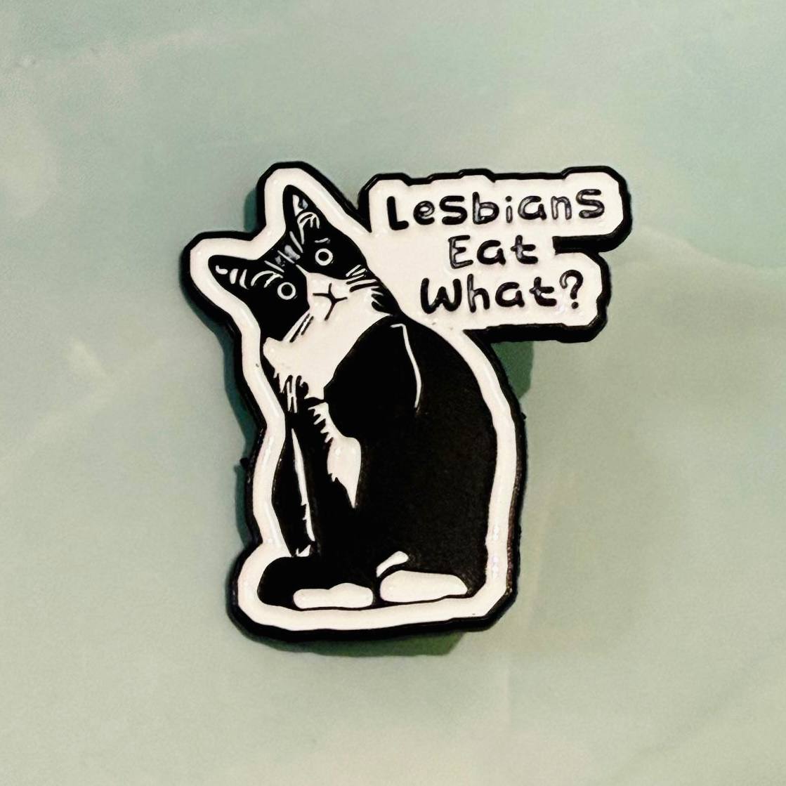 Sticker with a cat design and text 'Lesbians Eat What?' on a light gray background