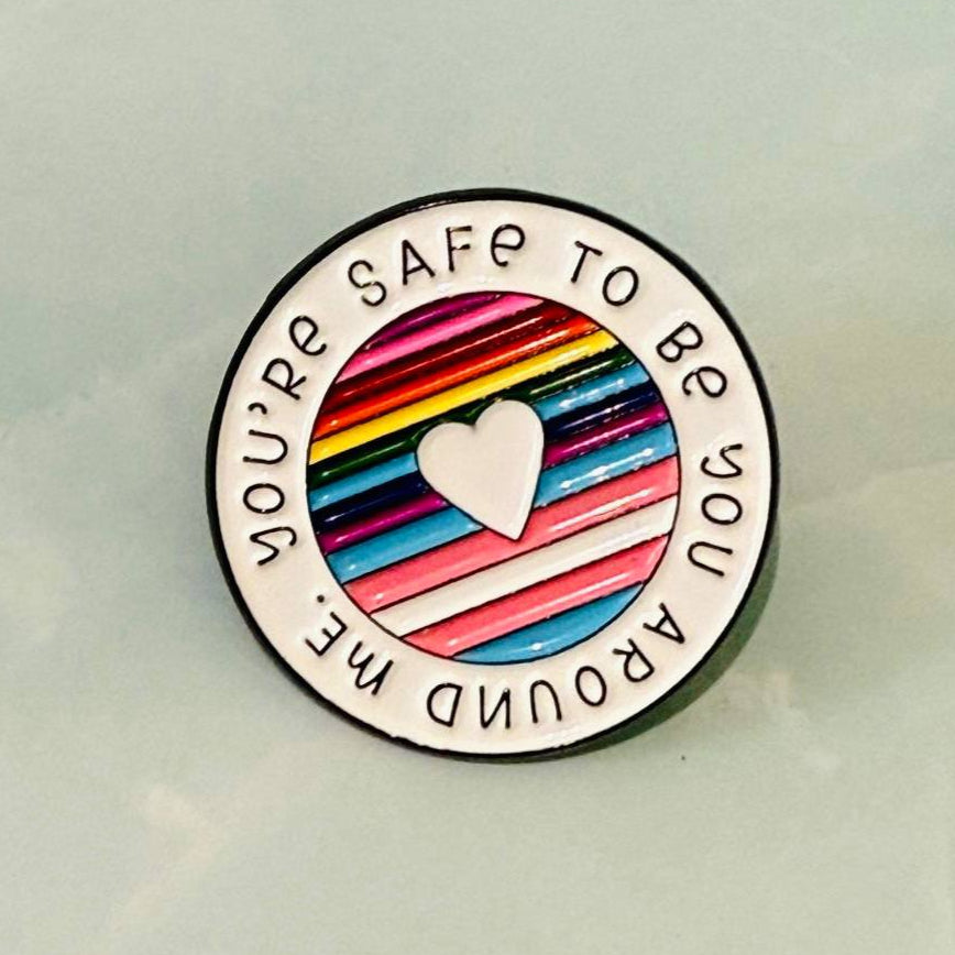 Round badge with rainbow heart and text 'You're safe to be you around me' on a light background