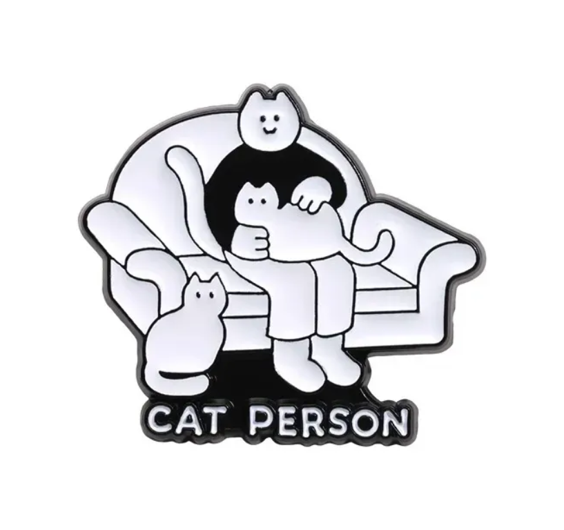 Enamel pin with cartoon character sitting on a couch with cats, labeled 'Cat Person'.