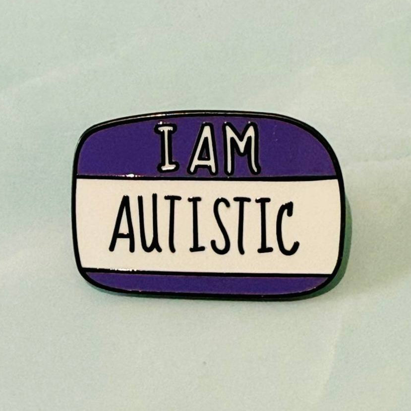 Enamel pin with 'I AM AUTISTIC' text on a white background