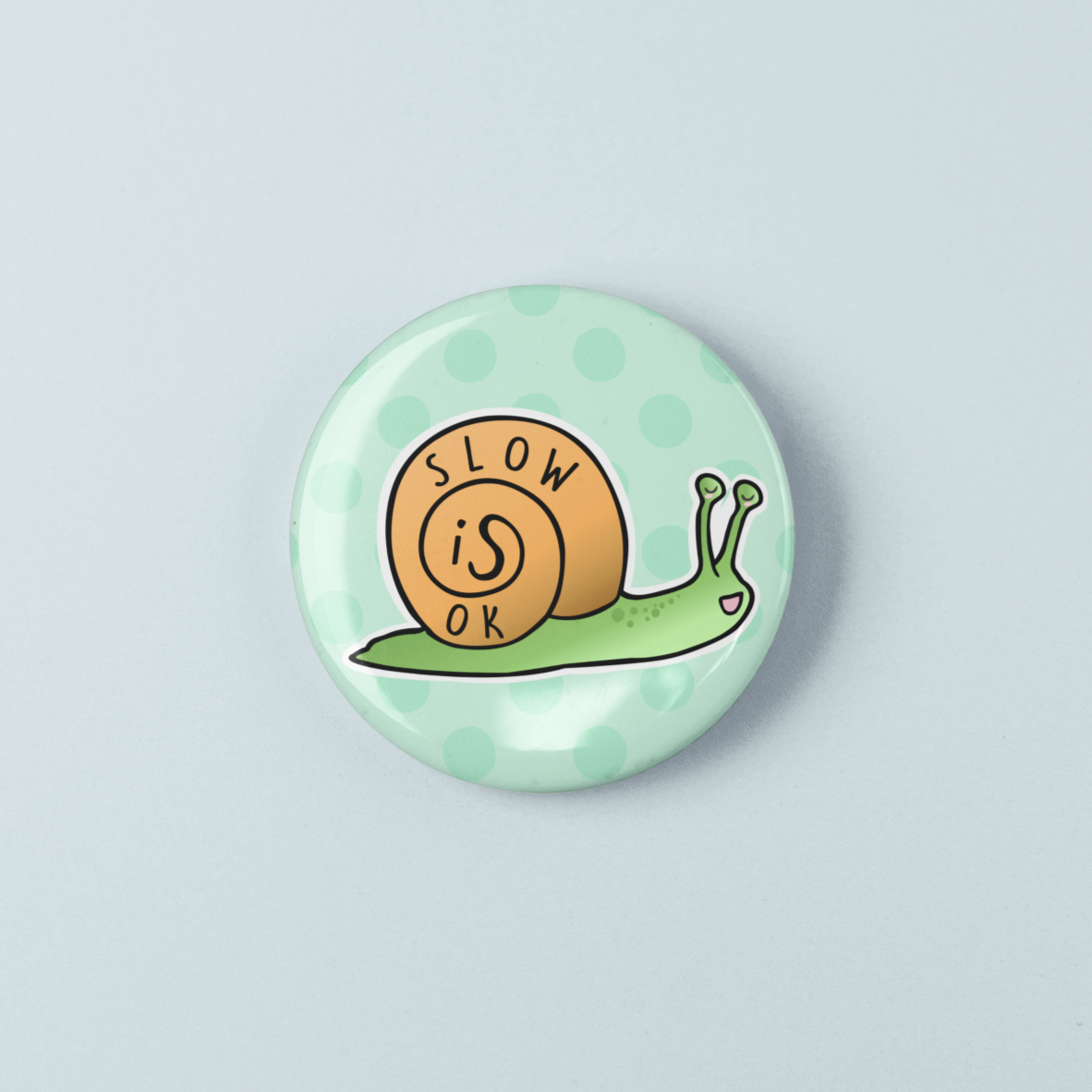 Button badge with a snail design and 'Slow is OK' text on a light blue background