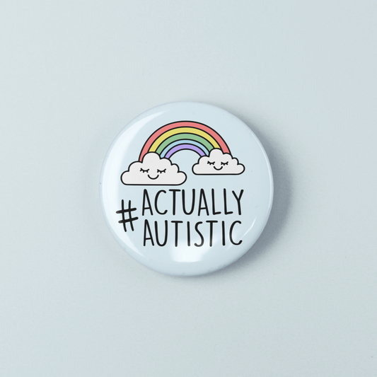 Button badge with '#Actually Autistic' text and rainbow design on a light gray background