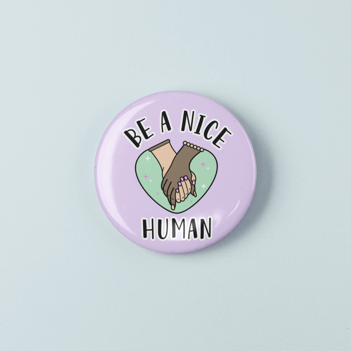 Button badge with 'Be a Nice Human' text and two hands on a light blue background