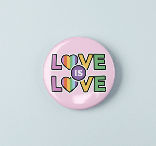 Pink button badge with 'LOVE IS LOVE' text in colorful letters on a light blue background
