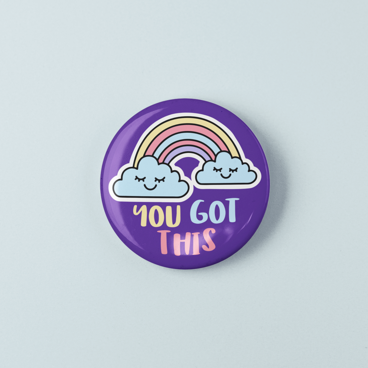 Button badge with rainbow and clouds design on a light gray background