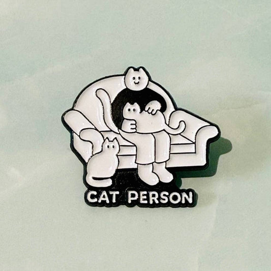 Pin with cartoon character sitting on a couch with a cat, labeled 'Cat Person' on a light gray background.
