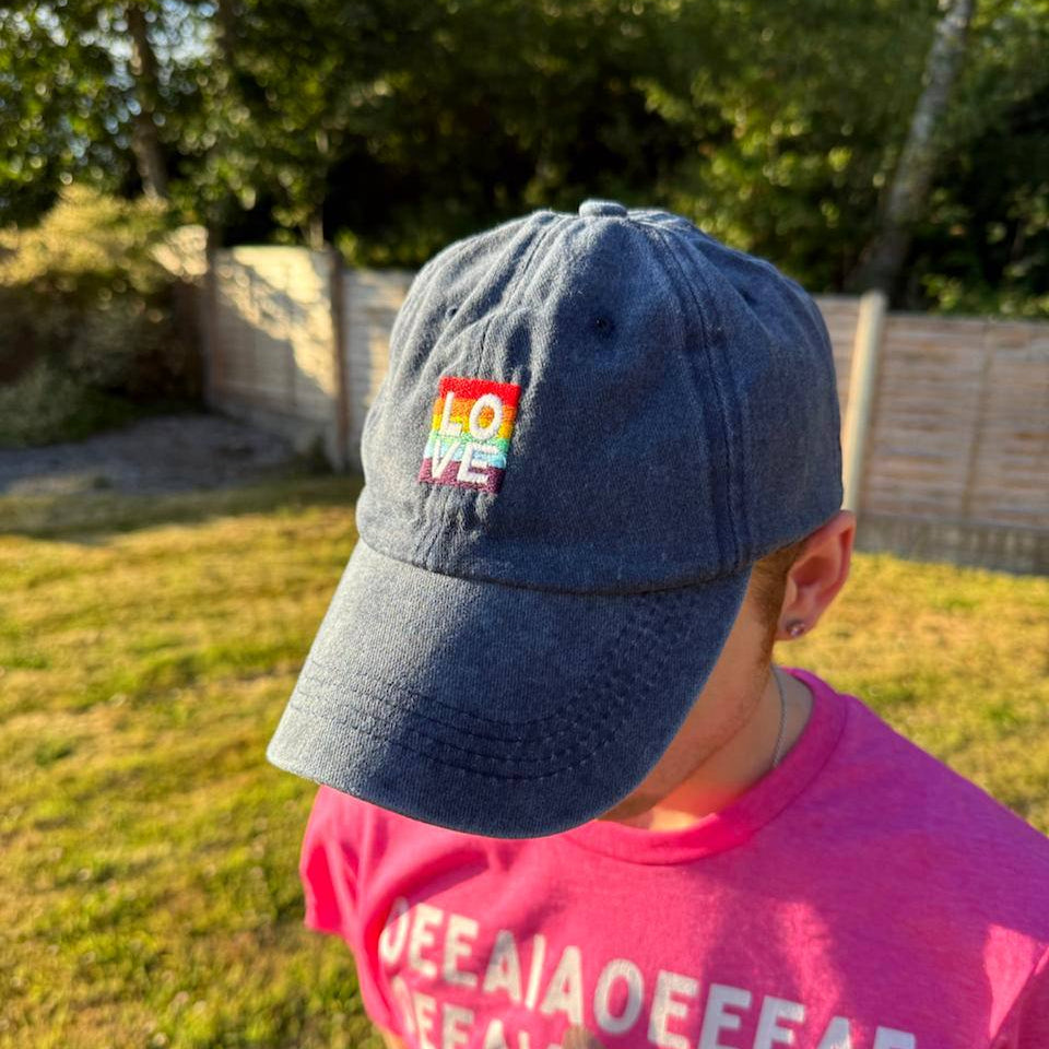 Person wearing a blue cap with a rainbow patch and pink shirt outdoors