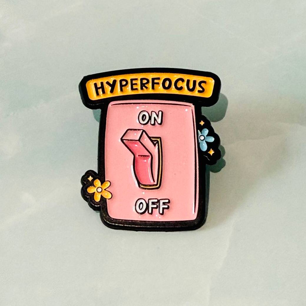 Enamel pin with 'Hyperfocus On Off' design on a light gray background