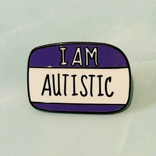 Enamel pin with 'I AM AUTISTIC' text on a white background