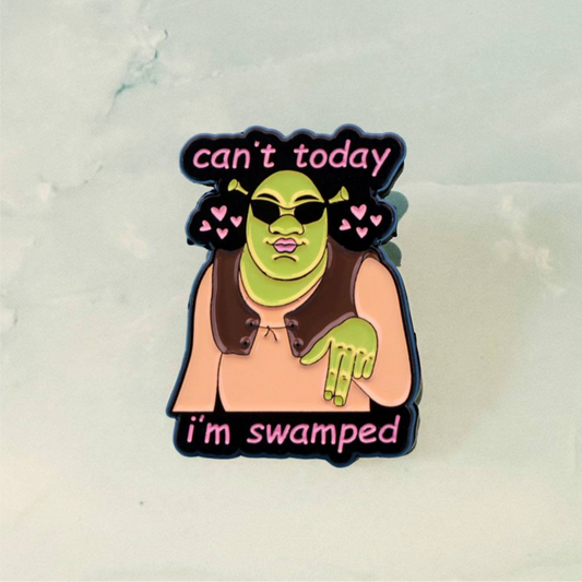Enamel pin with a character wearing sunglasses and text 'can't today, I'm swamped' on a light background